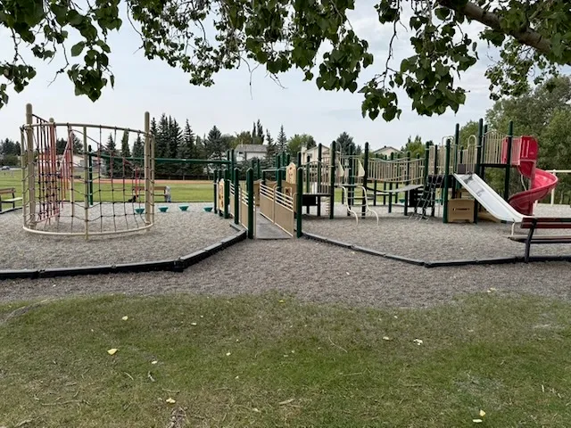 photo shows an overview of the current school playground from the East side; shows the rope and climbers on the left, ramp in the middle and bridge and slides to the right; metal is sun-faded